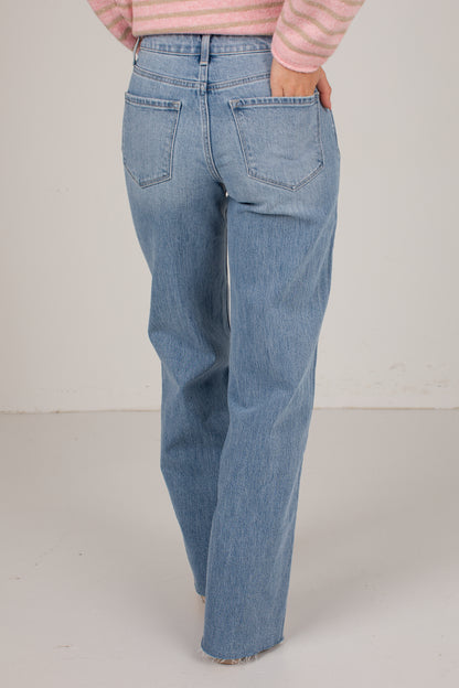 A person shown from the back wearing light-wash blue jeans and a pink striped long-sleeve top, standing against a plain light gray studio background.