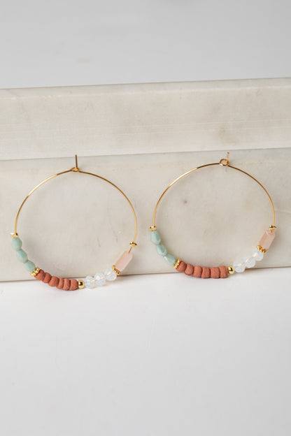 Gold hoop earrings with colorful beads on a light surface