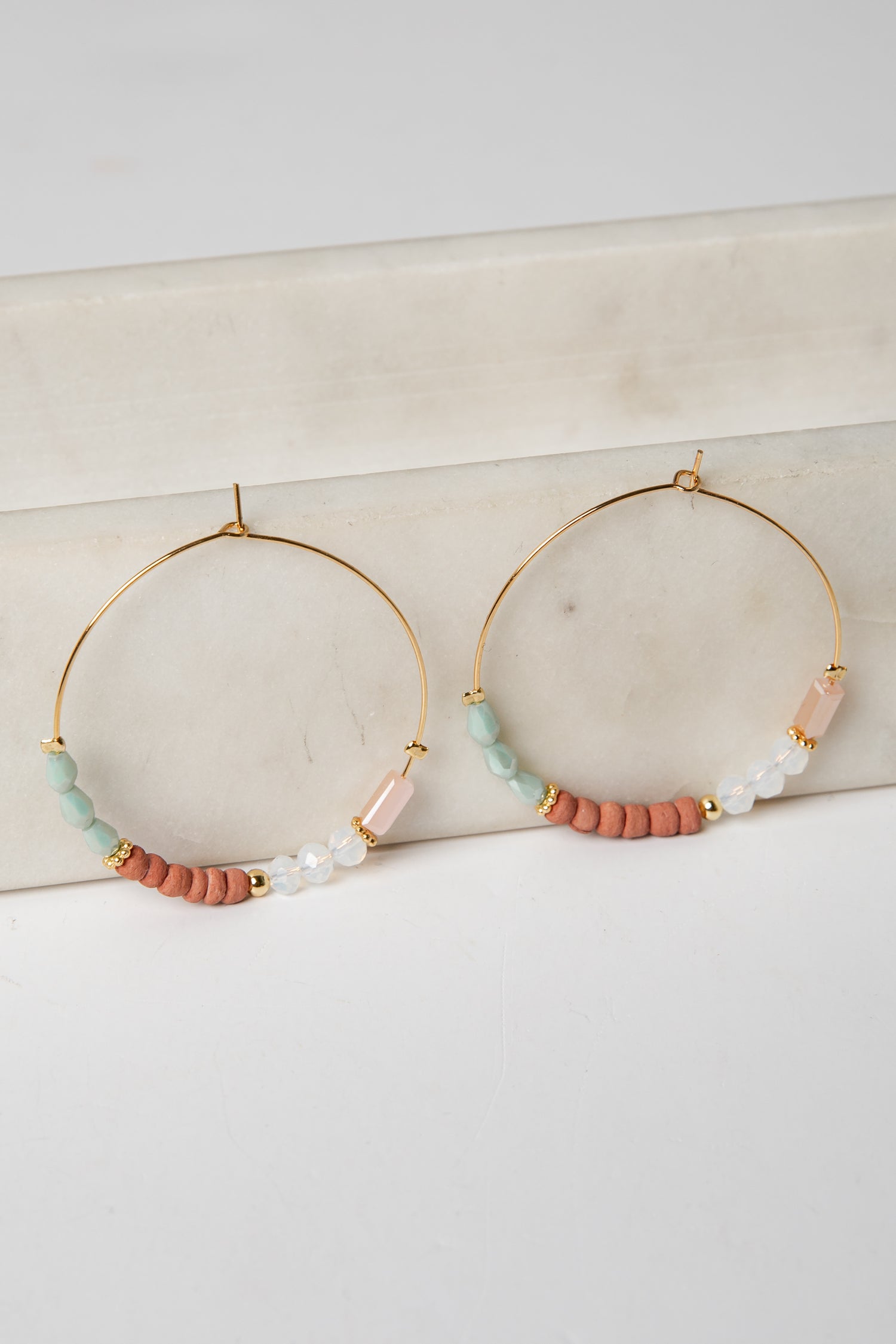 Gold hoop earrings with colorful beads on a marble surface