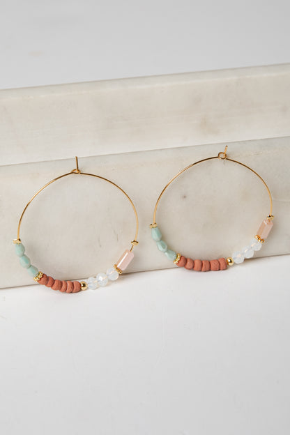 Gold hoop earrings with colorful beads on a marble surface