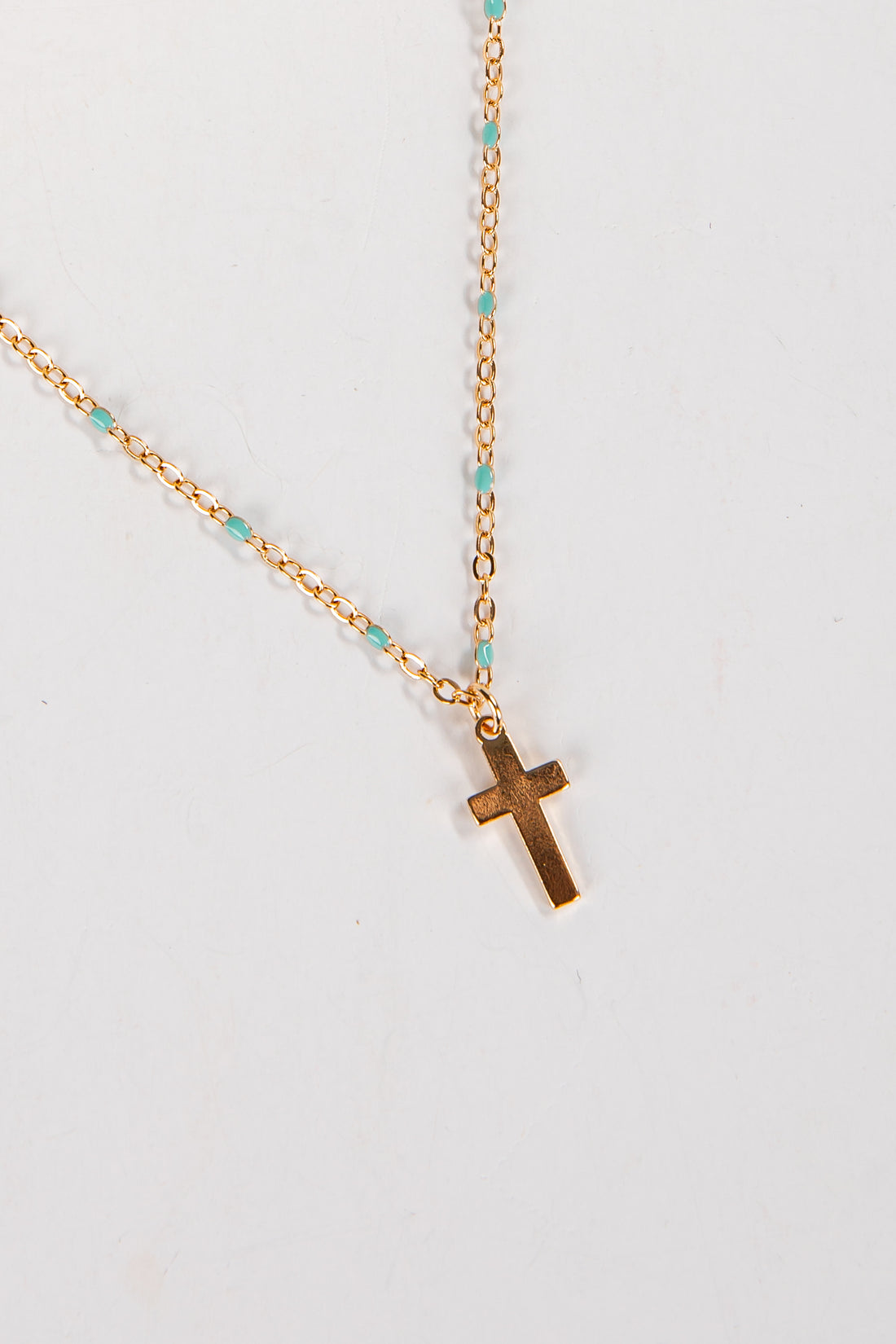 Gold necklace with a cross pendant on a light gray background
