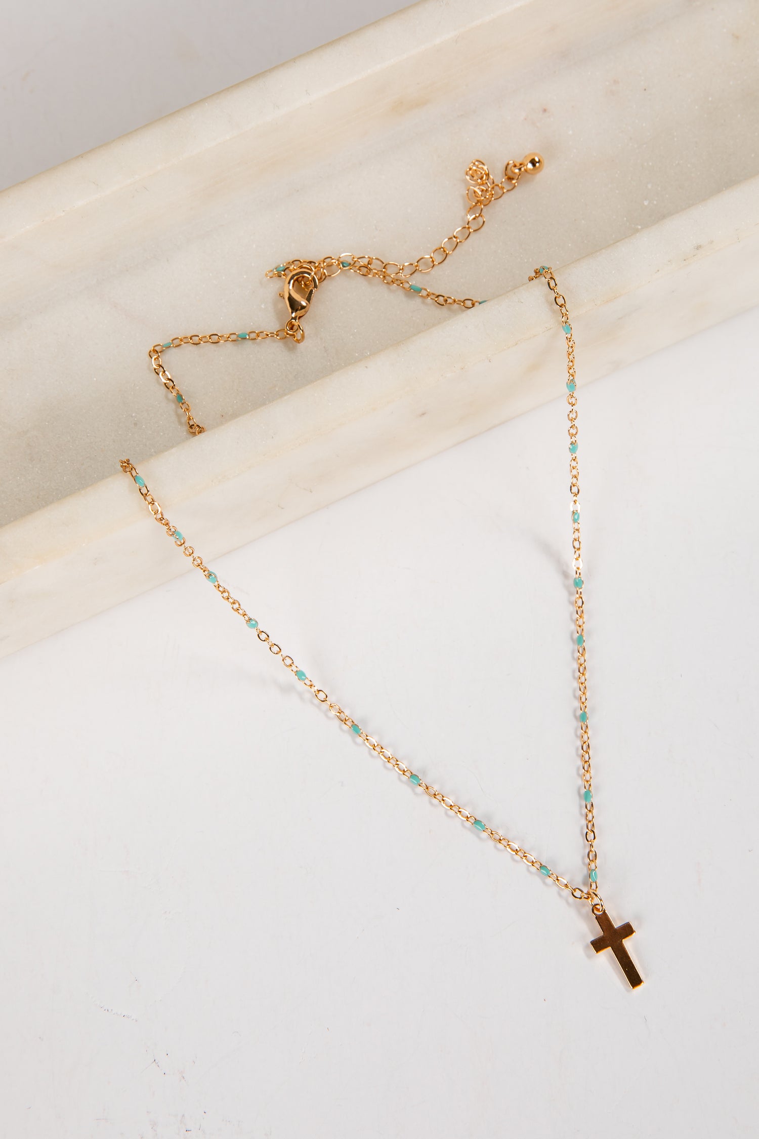 Gold necklace with a cross pendant on a marble surface