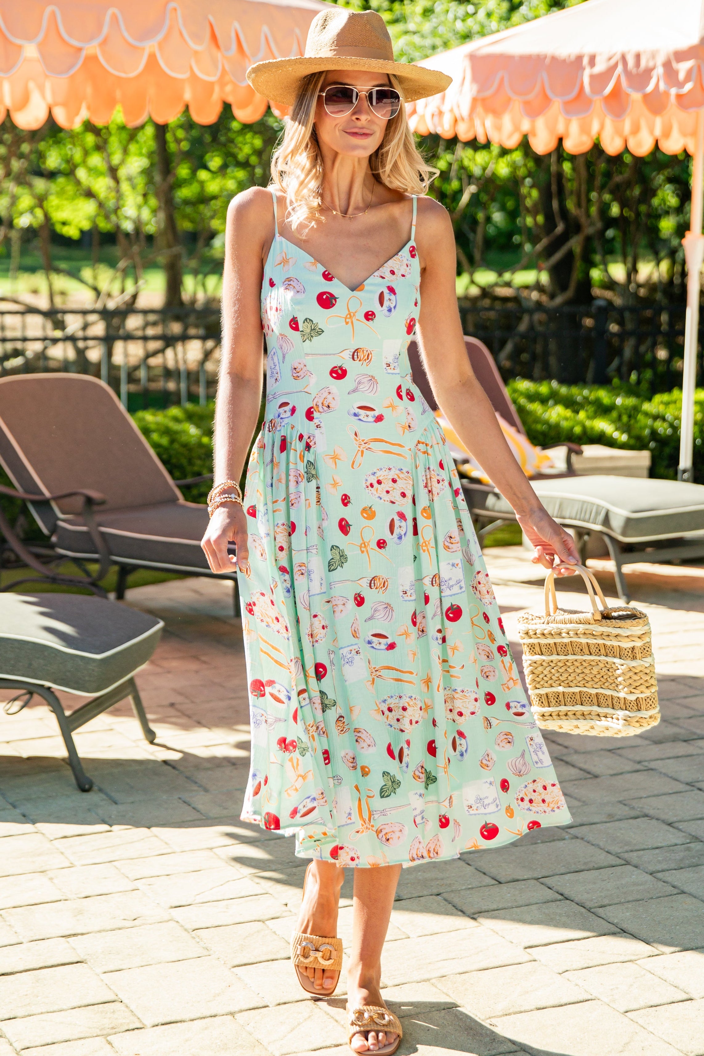 Woman in a floral dress standing under peach-colored umbrellas in a sunlit outdoor setting.