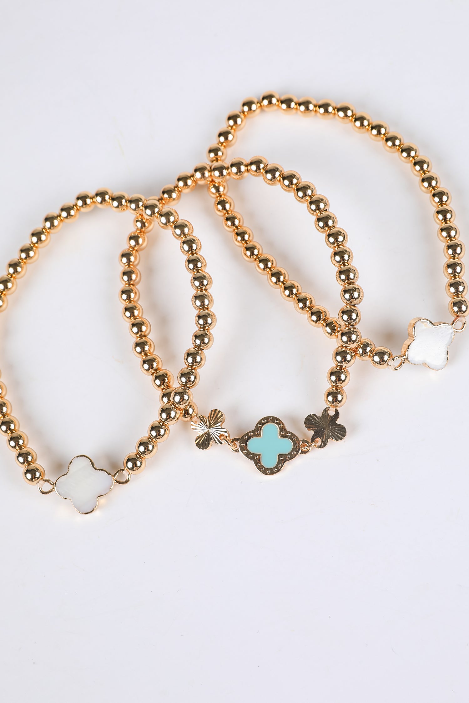 Three gold beaded bracelets with clover-shaped charms on a light background