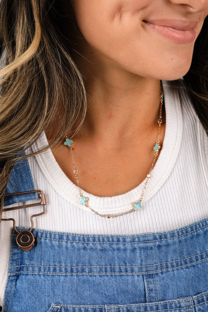 Close-up of a person wearing a necklace with turquoise heart pendants, white top, and blue denim overalls.