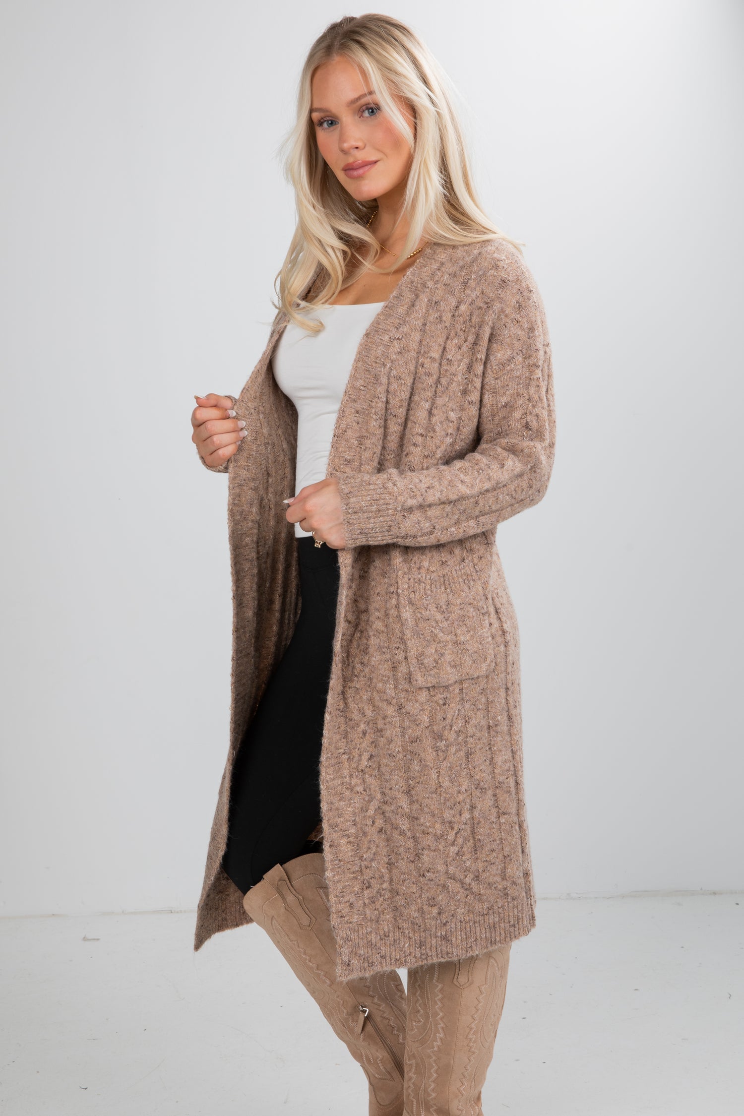 Woman wearing a long beige cardigan over a white top and black skirt on a white background