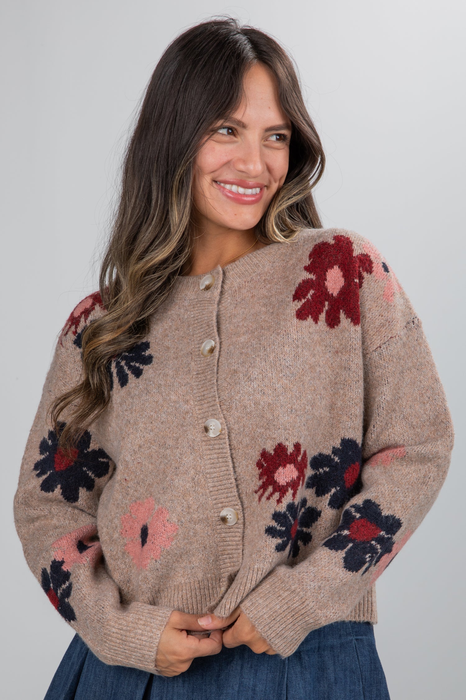 Woman wearing a beige cardigan with floral patterns on a plain background