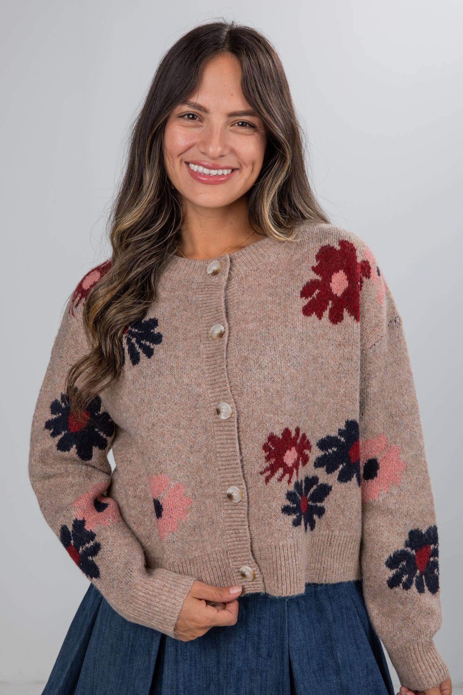 Woman wearing a beige cardigan with floral patterns on a plain background