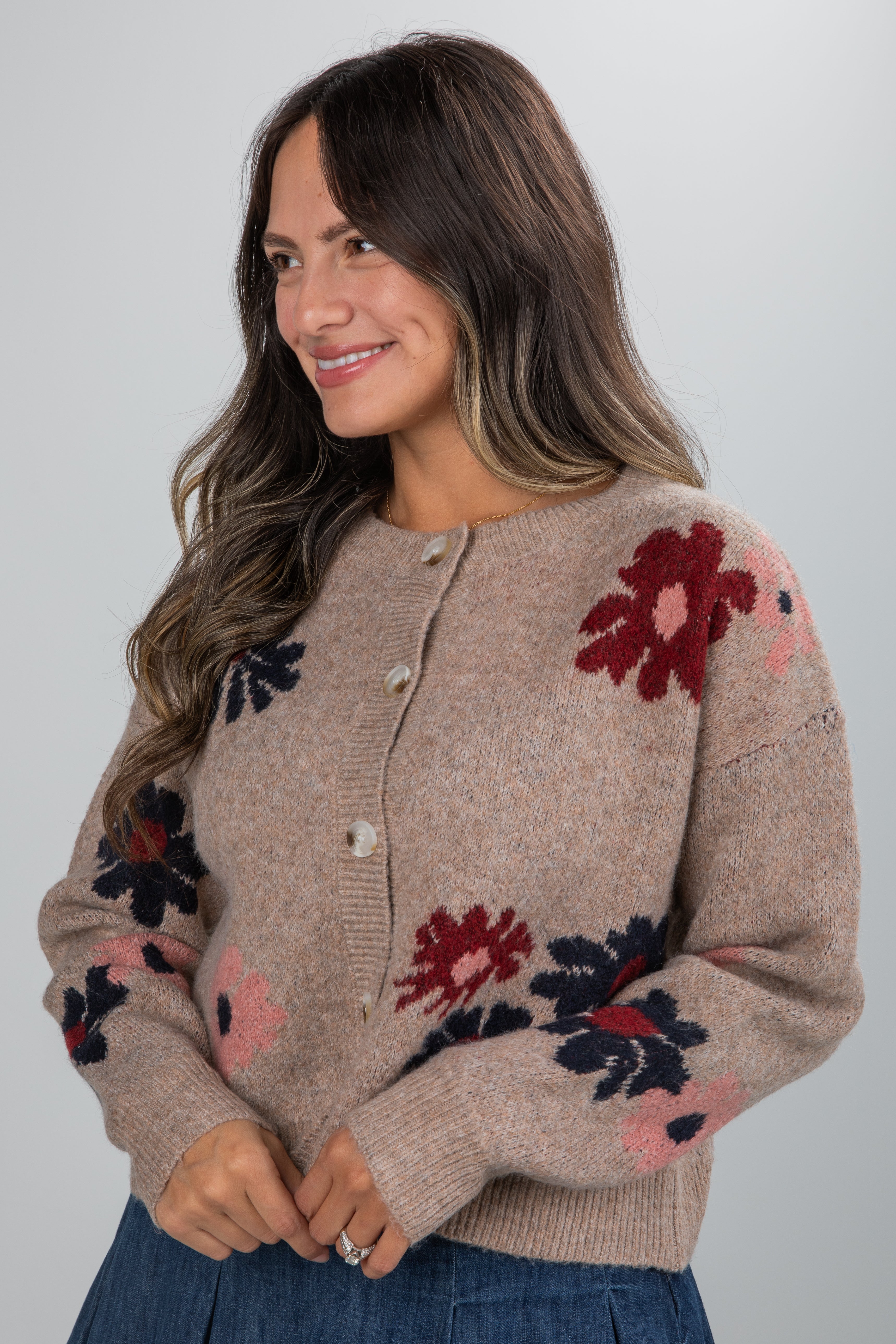 Woman wearing a beige cardigan with floral patterns on a plain background