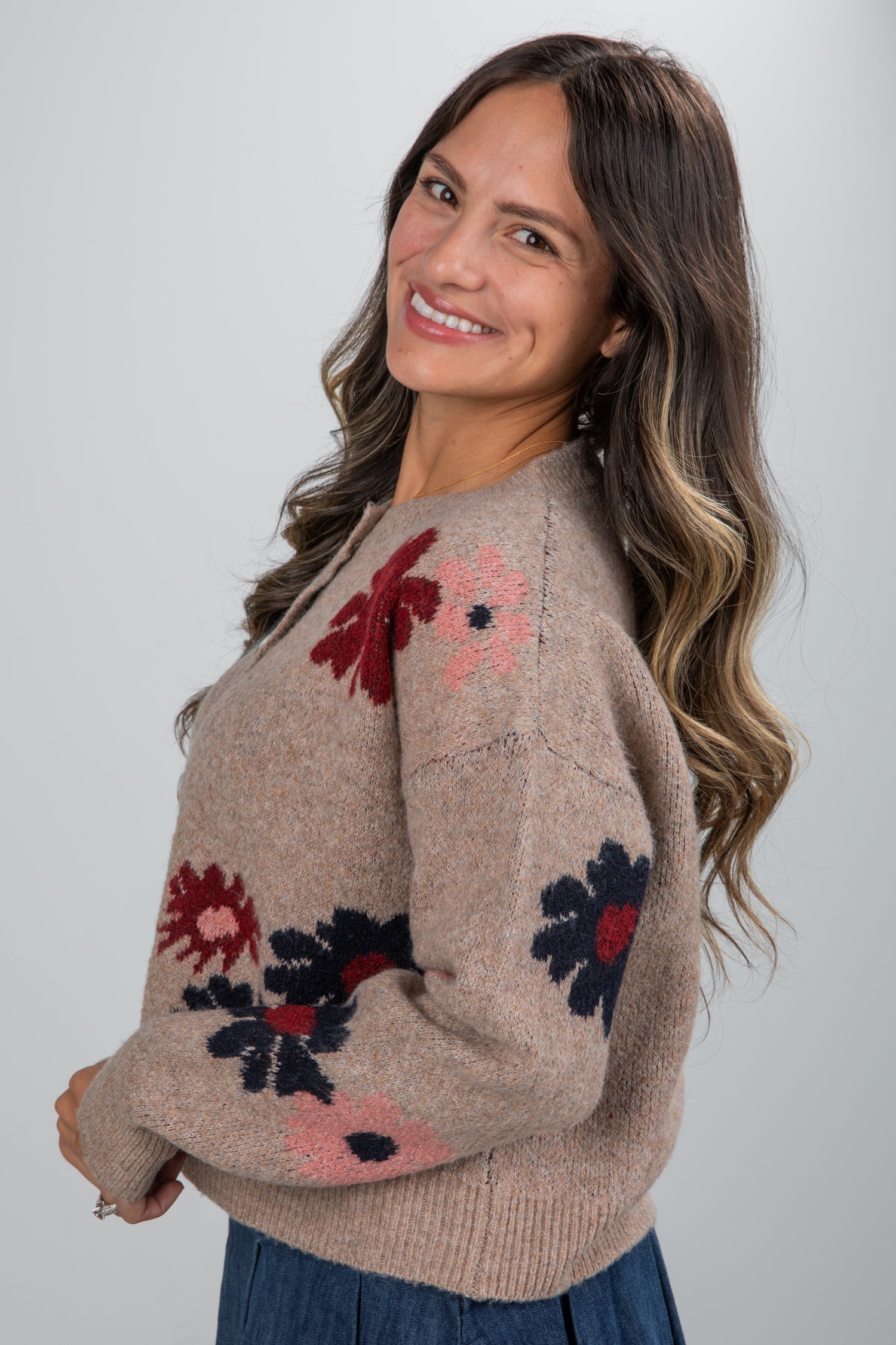Woman wearing a beige sweater with floral patterns on a plain background