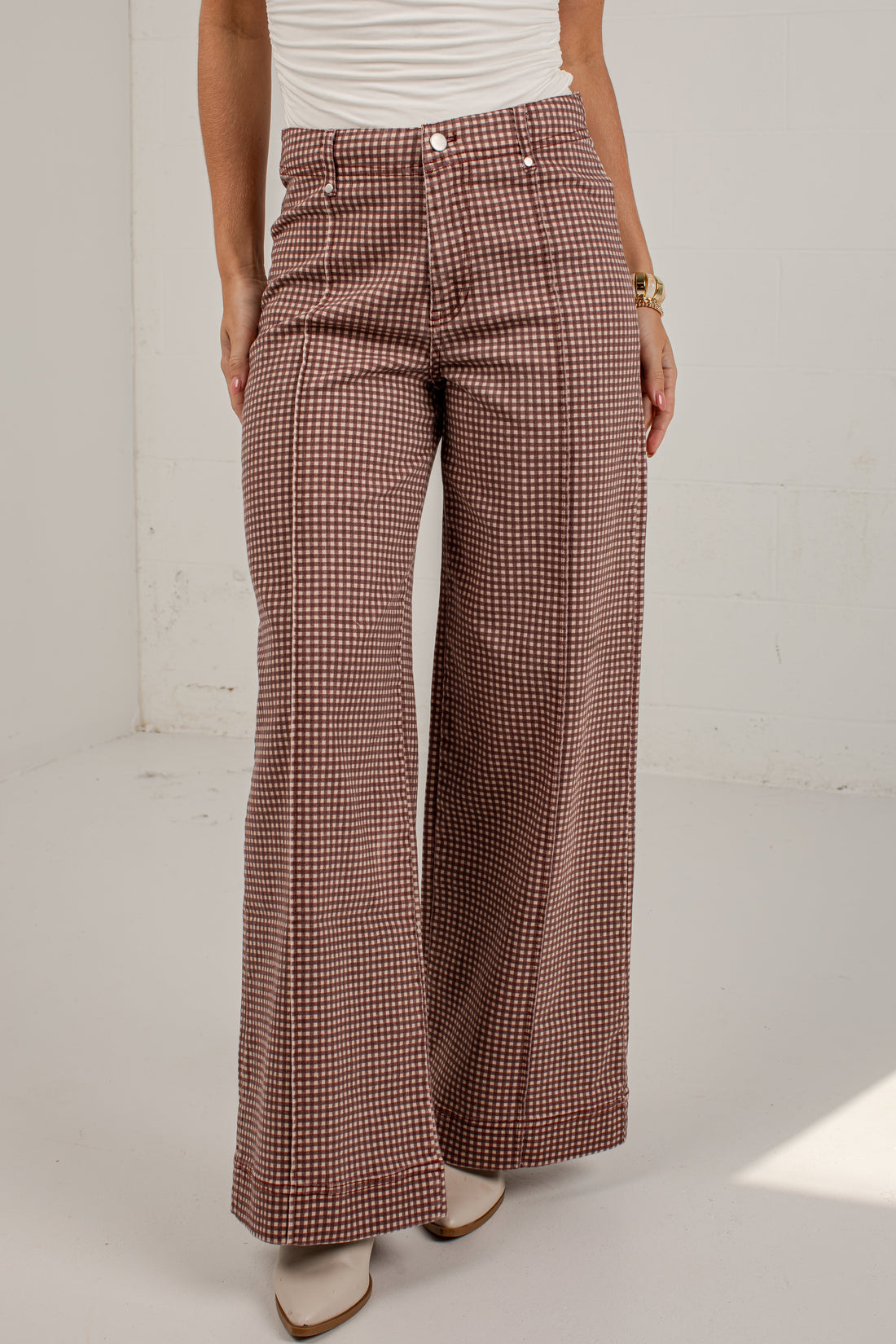 A model wearing high-waisted, wide-leg trousers with a brown and beige houndstooth pattern, paired with a white top and beige boots.