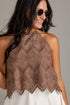 A woman wearing a brown eyelet lace halter top and white bottoms, photographed against a plain light gray studio background.