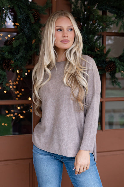 Woman wearing a beige sweater and blue jeans standing in front of a decorated Christmas tree.