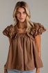 A close-up of a woman wearing a brown smocked-shoulder top with dramatic ruffled puff sleeves and a gathered neckline.