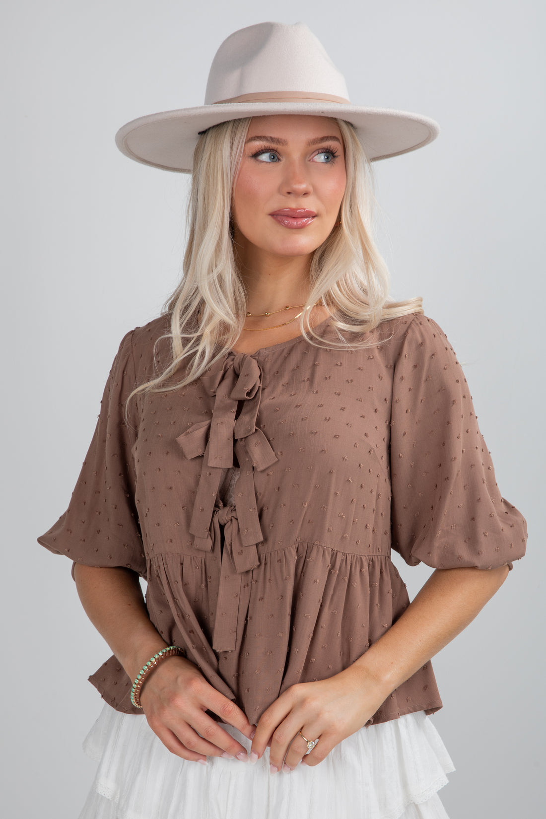 Woman wearing a brown blouse with ruffles and a beige hat on a plain background
