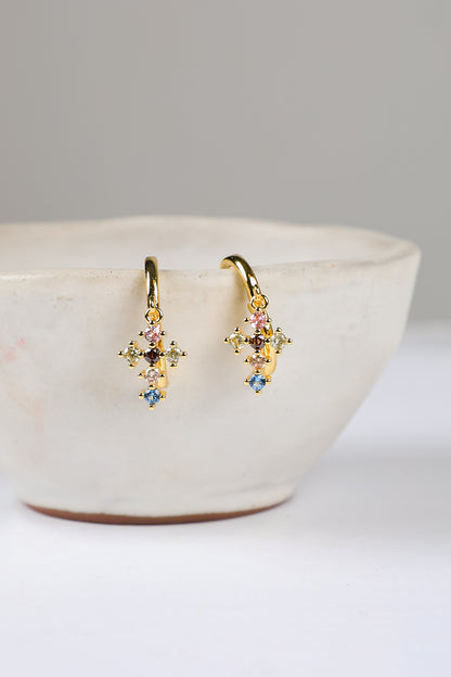 Gold earrings with colorful stones on a white bowl