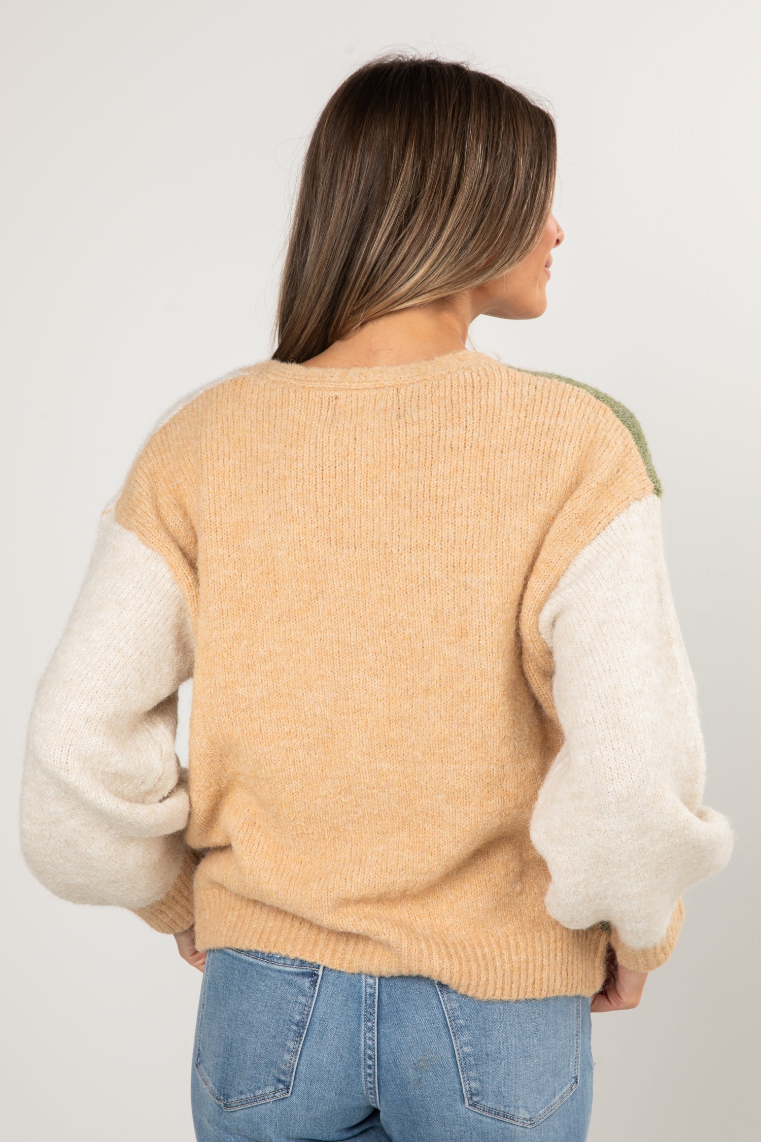 Person wearing a beige sweater with white sleeves on a plain background