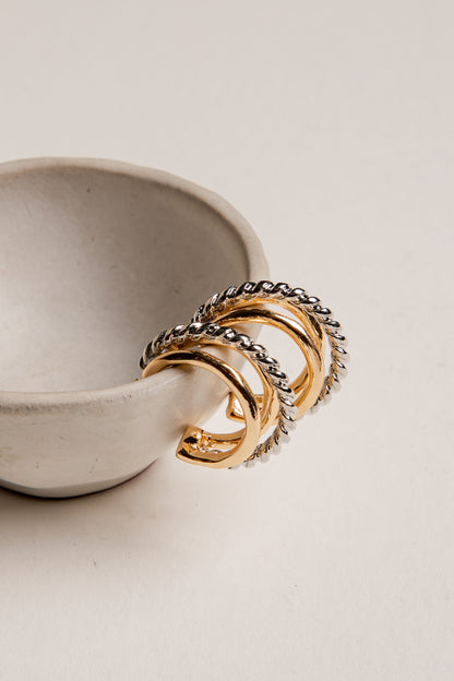 Three gold rings with braided designs on a white ceramic dish.