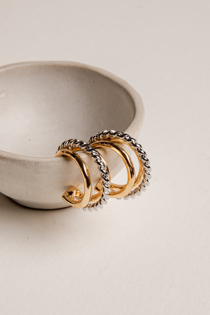 Gold and silver hoop earrings on a light beige surface with a ceramic bowl in the background.