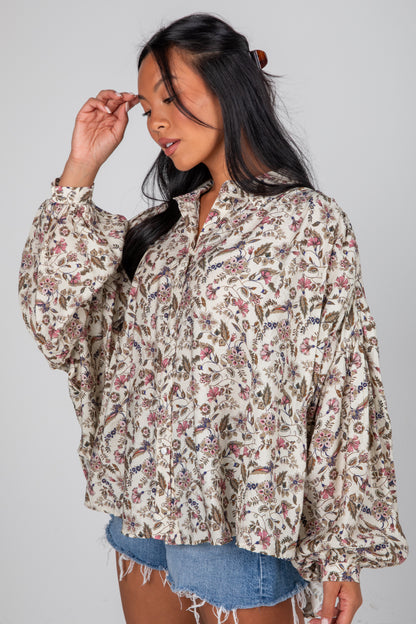 Woman wearing a floral blouse and denim shorts on a gray background