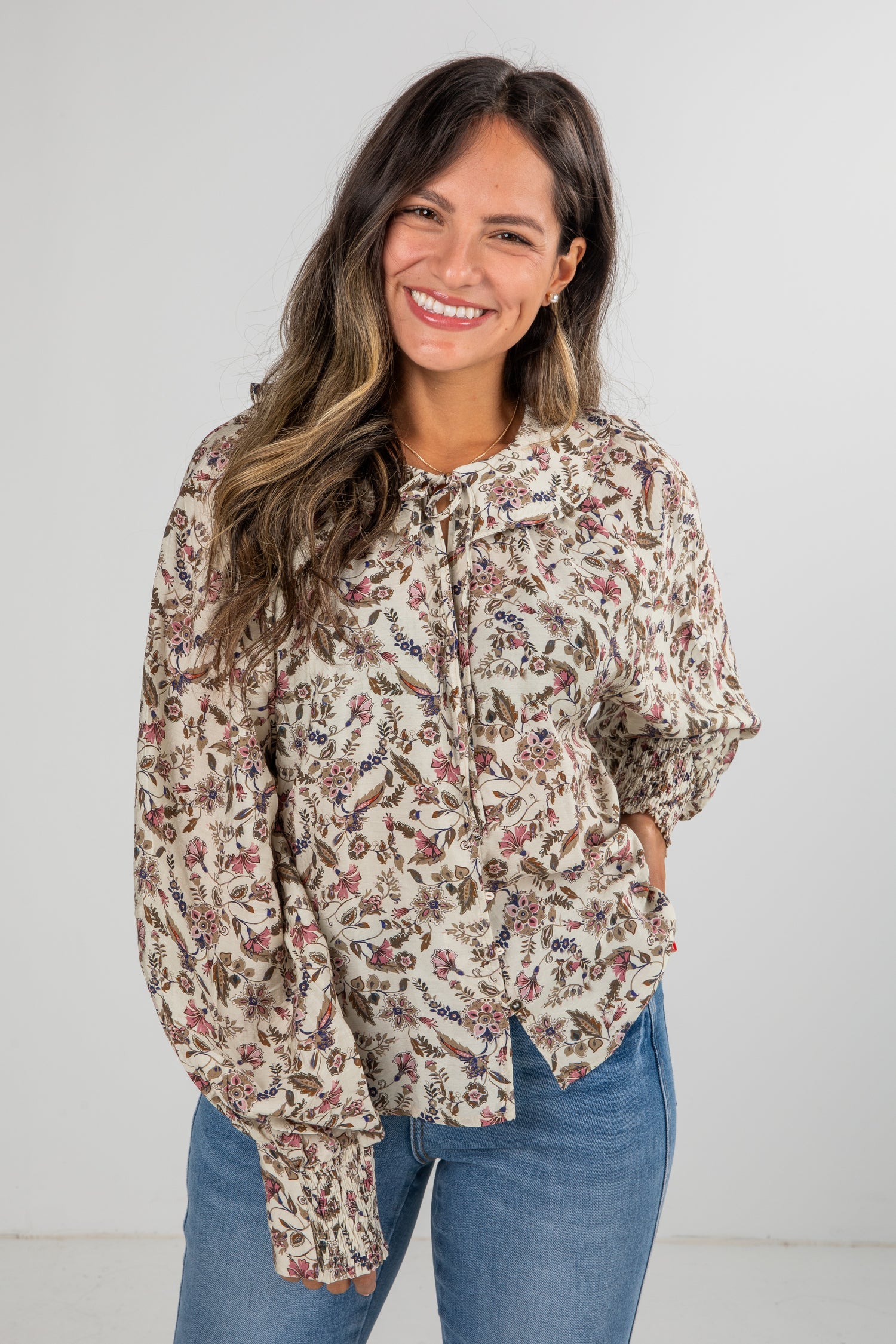 Woman wearing a floral blouse and blue jeans against a white background