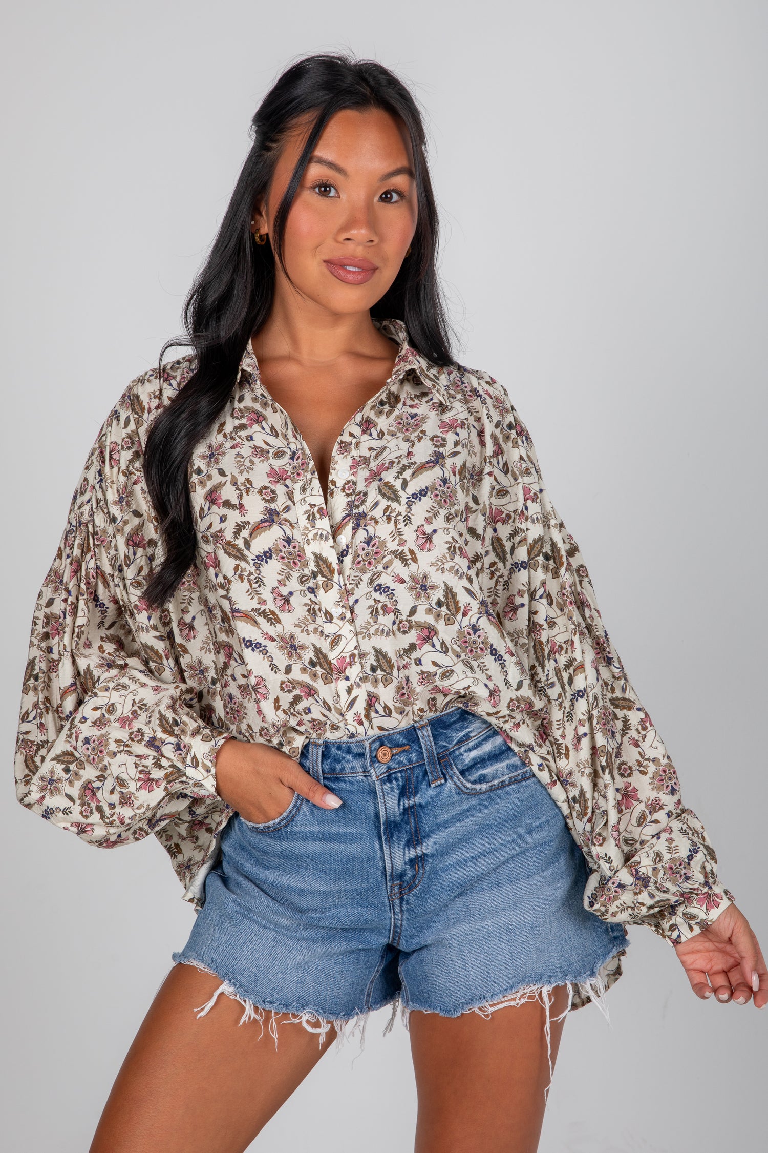 Woman wearing a floral blouse and denim shorts on a plain background
