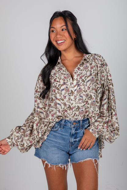 Woman wearing a floral blouse and denim shorts on a gray background