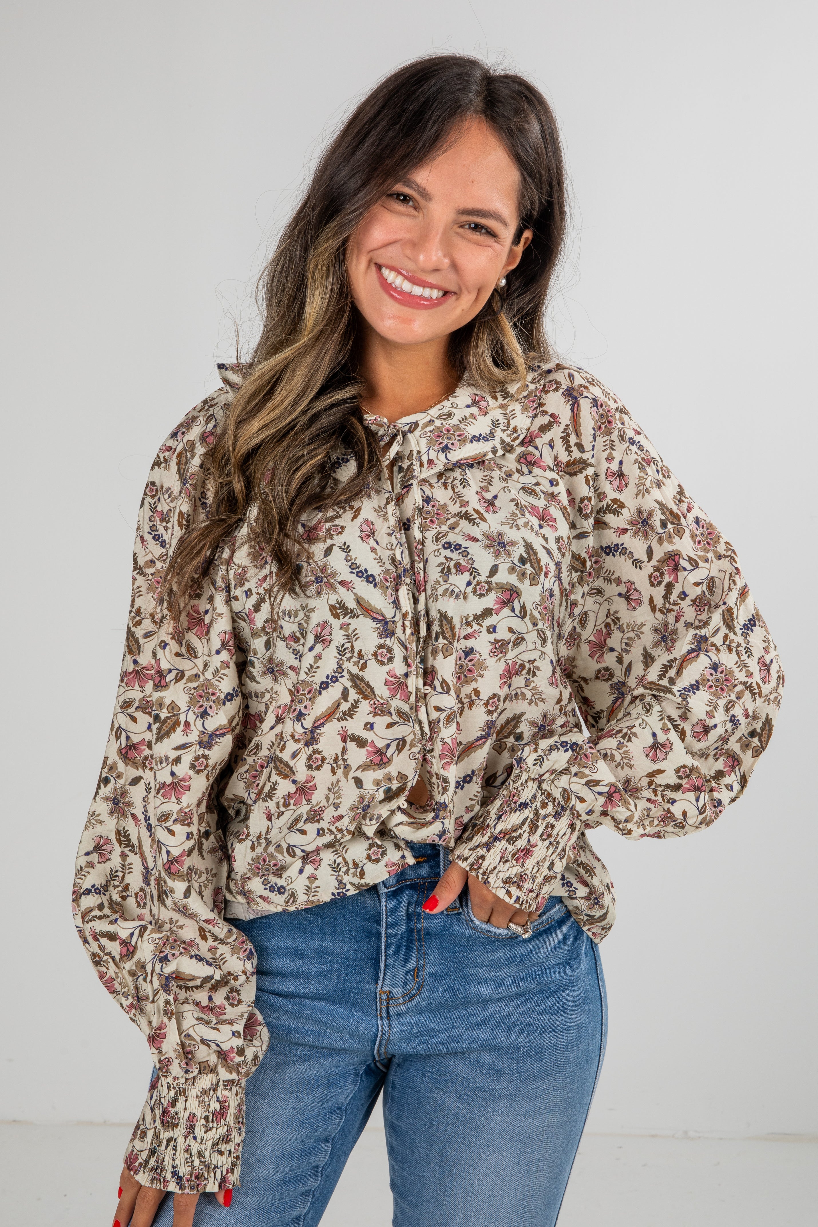 Woman wearing a floral blouse and blue jeans against a white background