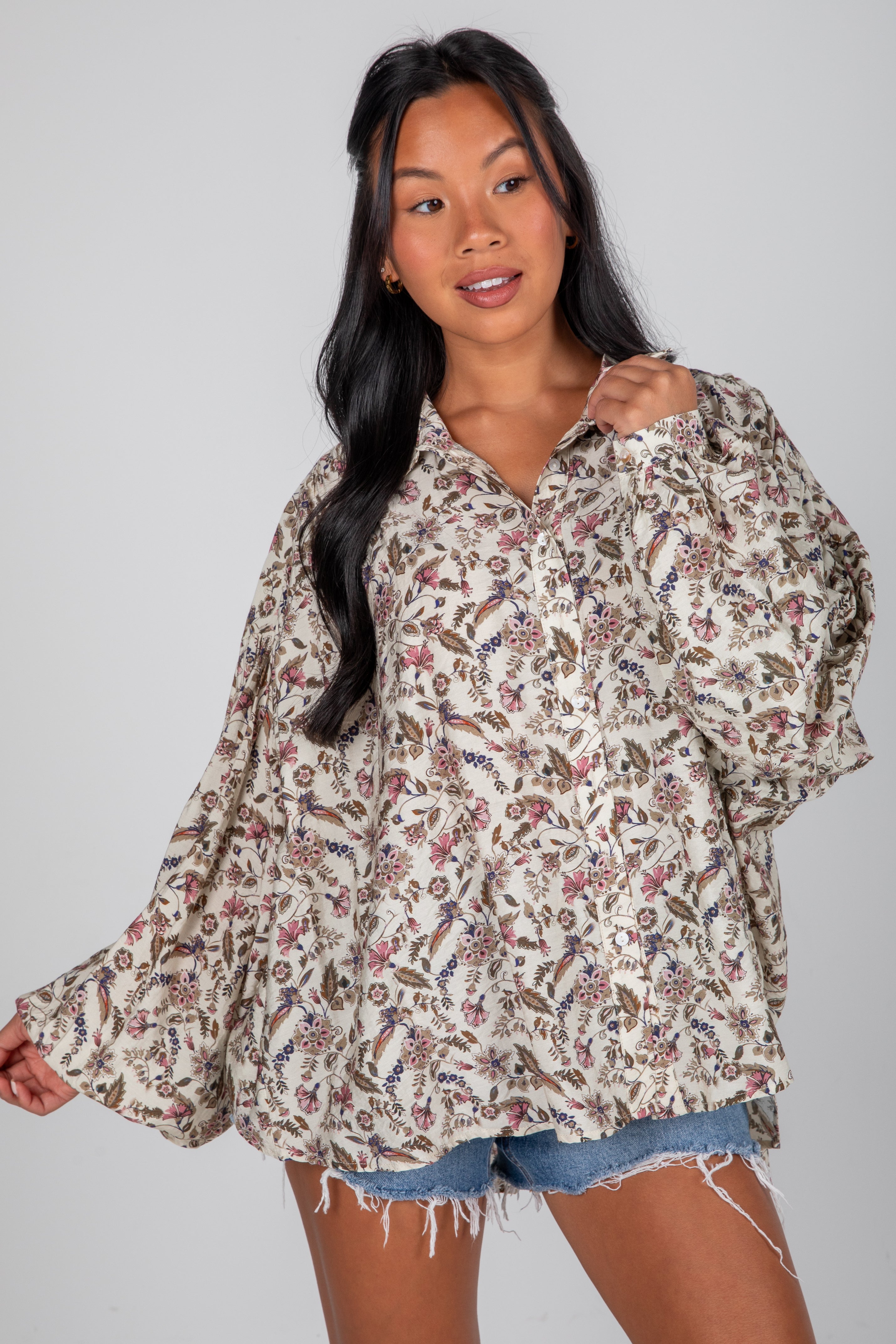 Woman wearing a floral blouse and denim shorts on a gray background