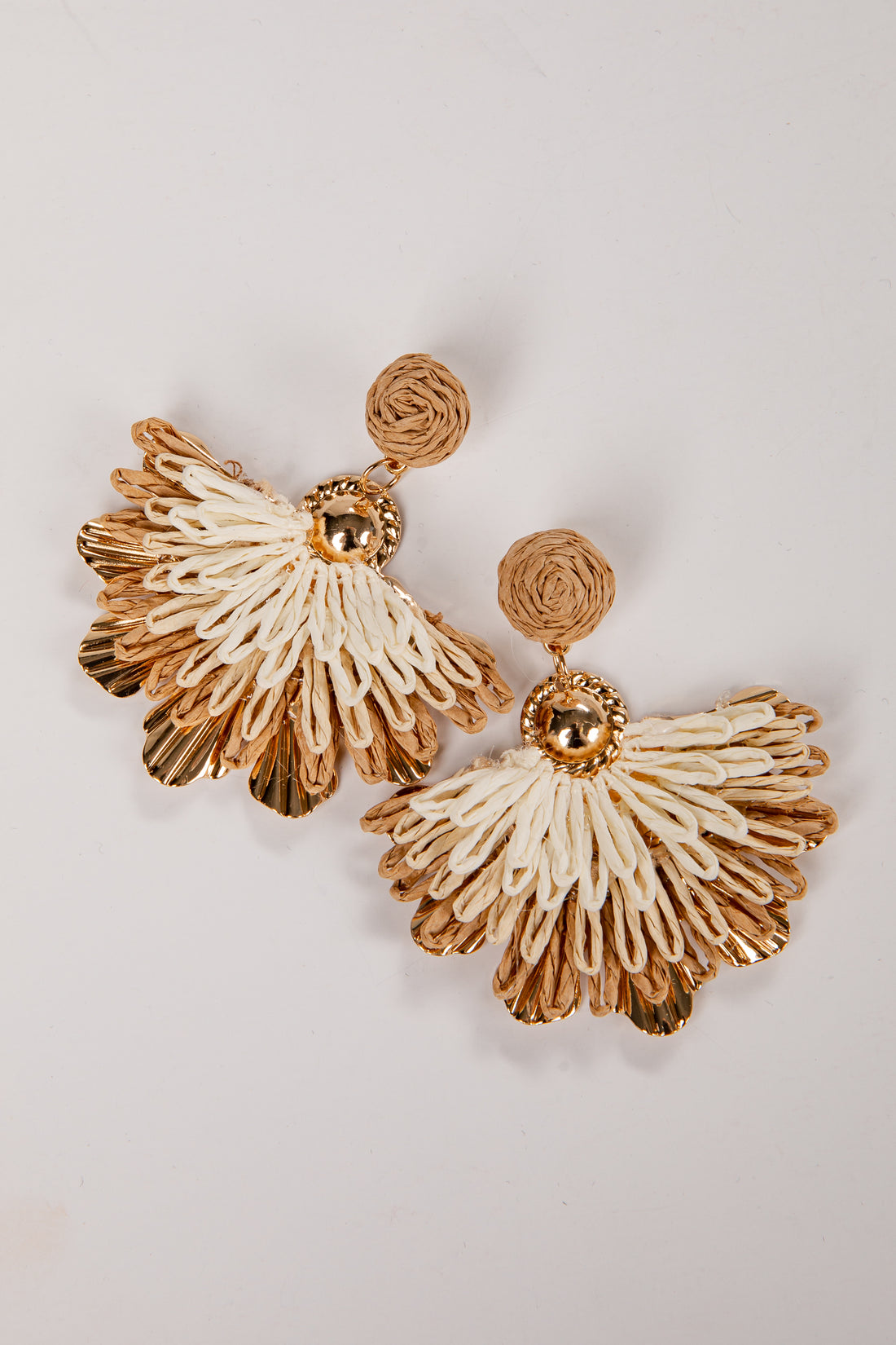 Gold and beige raffia earrings on a light gray background