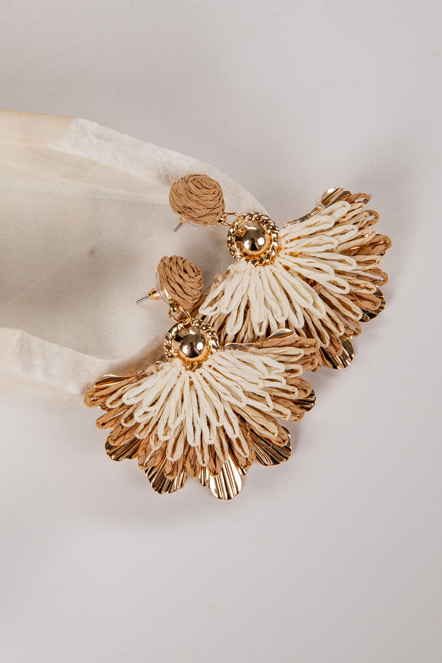 Pair of gold and white earrings on a light fabric background