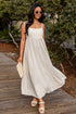 Woman in a white dress standing on a wooden path with greenery in the background