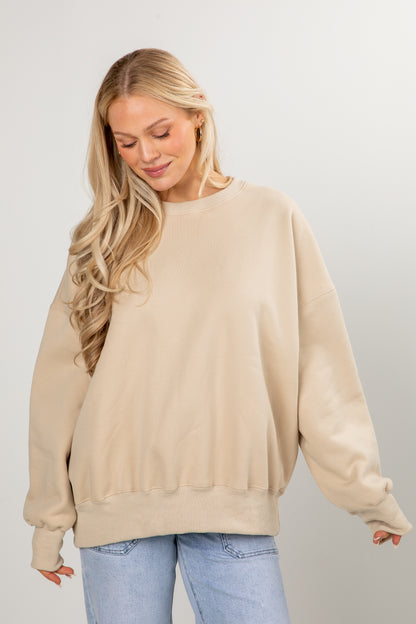 Woman wearing a beige sweater and light blue jeans against a plain background