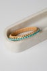 Gold bracelet with turquoise stones on a white surface