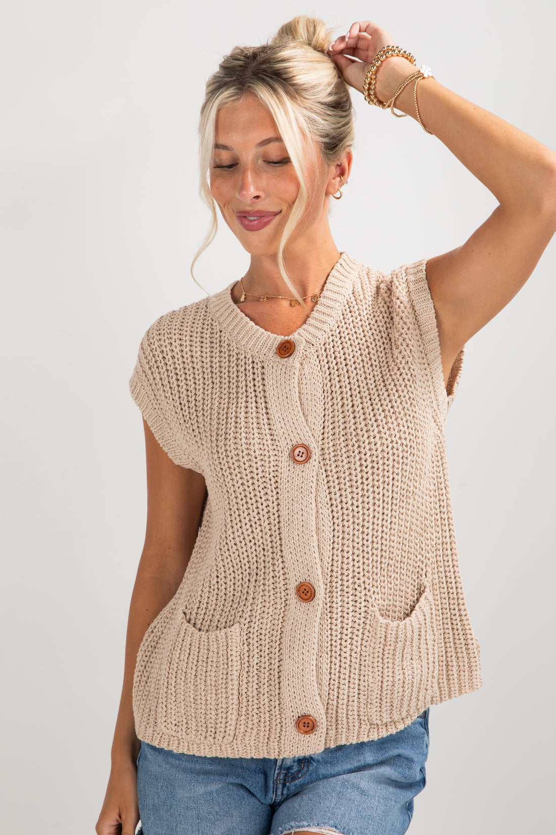 Woman wearing a beige knitted vest with brown buttons on a plain background