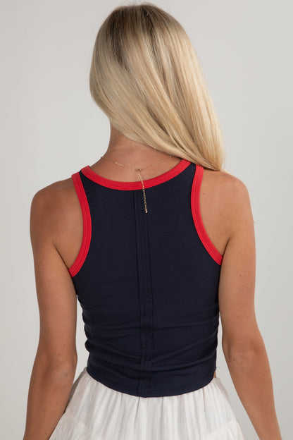 Person wearing a navy tank top with red trim on a plain background