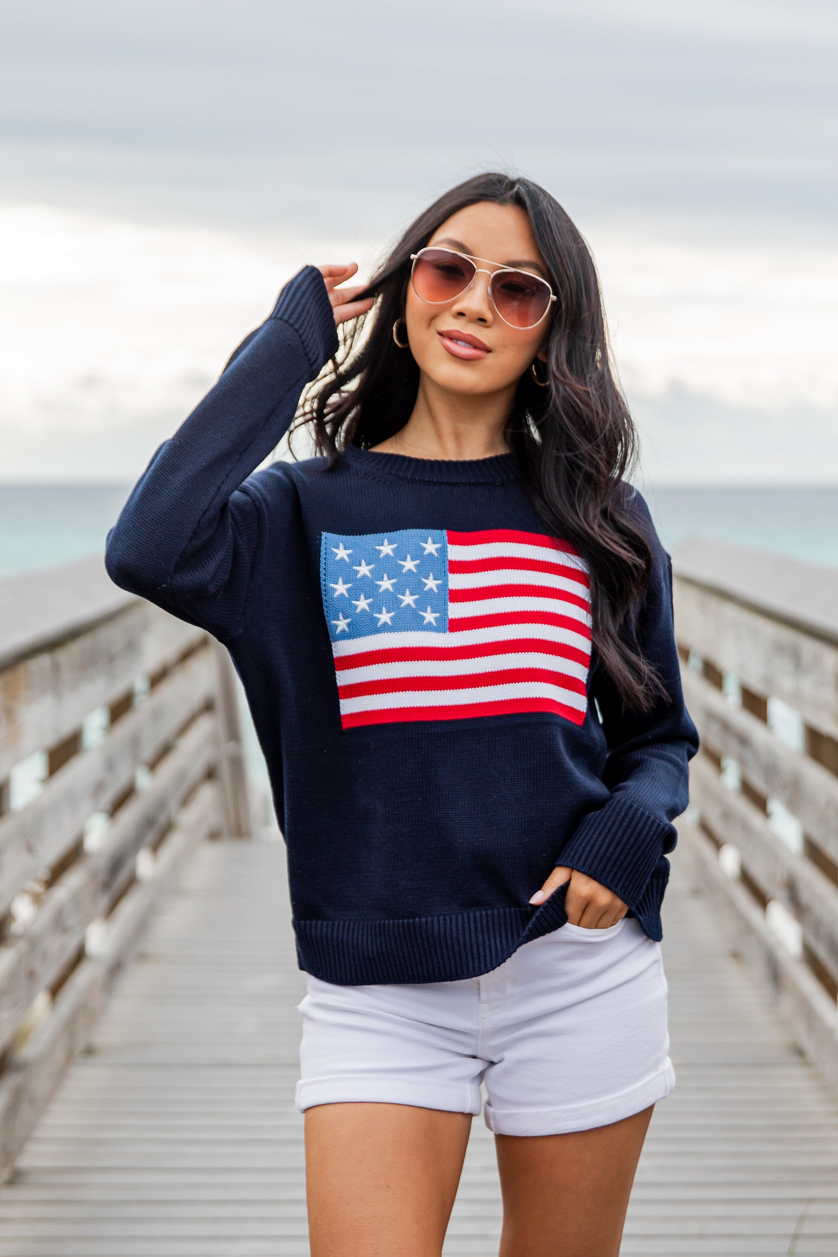 Woman wearing a navy blue sweater with an American flag design on a wooden pier.