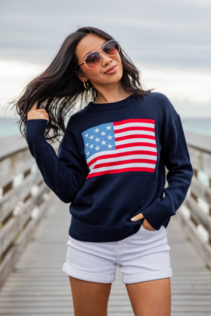 Woman wearing a navy sweater with an American flag design on a wooden pier.