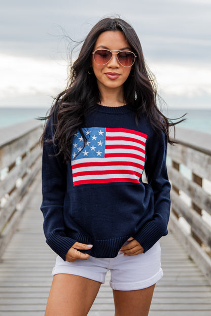 Woman wearing a navy blue sweater with an American flag design on a wooden pier.
