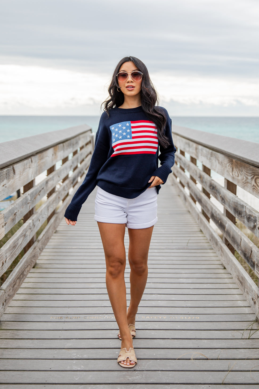 Woman wearing a navy sweatshirt with an American flag design on a wooden pier.