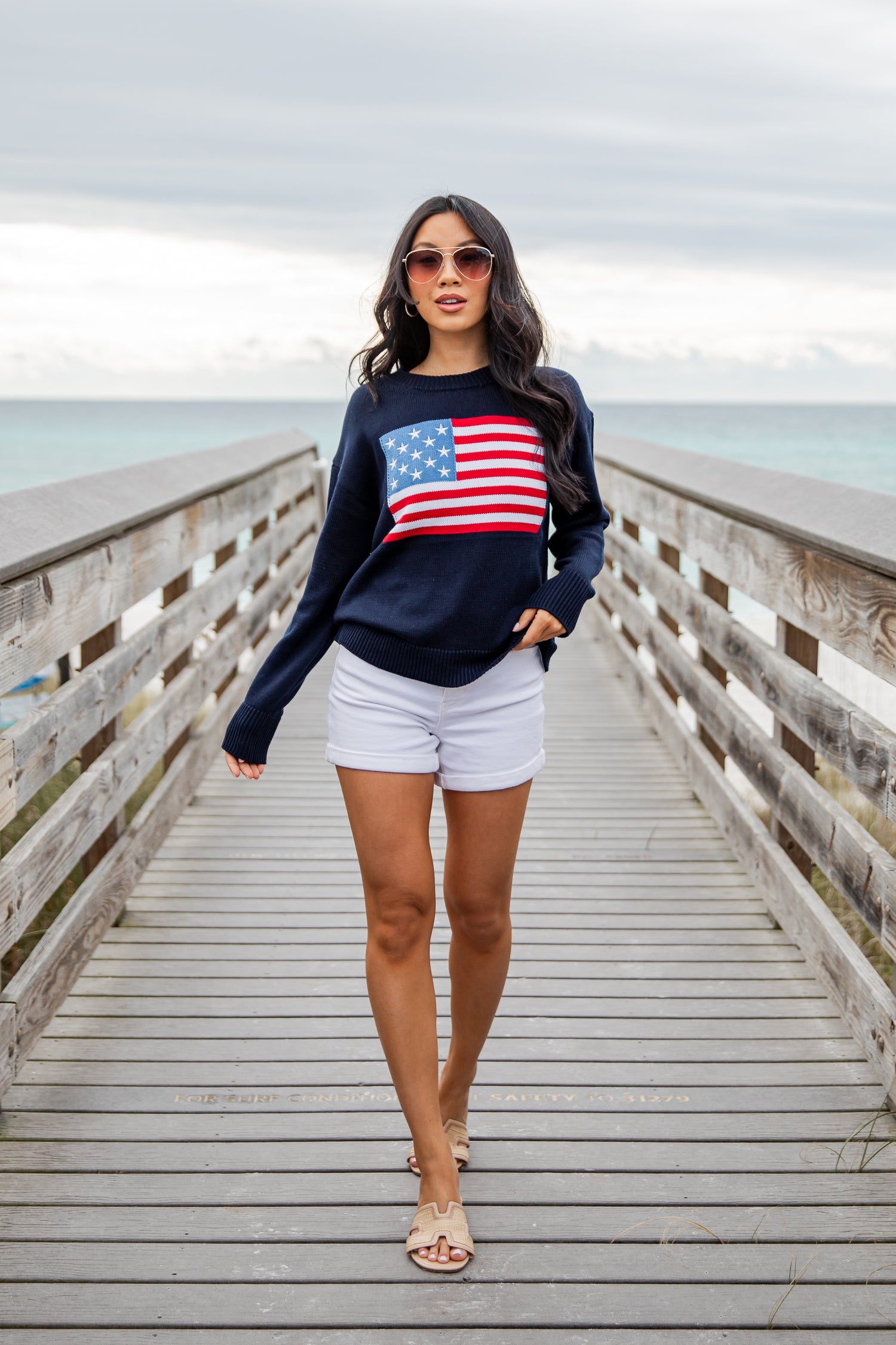 Woman wearing a navy sweatshirt with an American flag design on a wooden pier.
