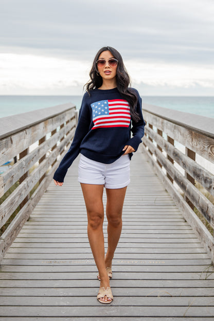 Woman wearing a navy sweatshirt with an American flag design on a wooden pier.