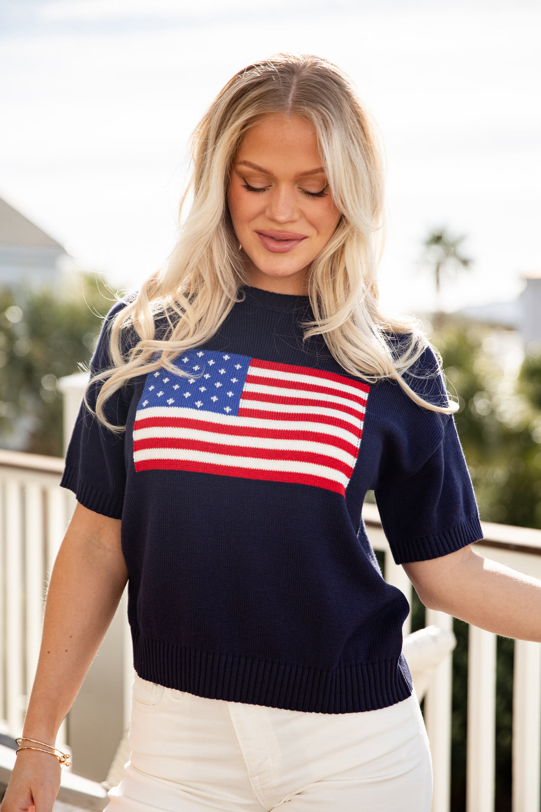 Woman wearing a navy sweater with an American flag design outdoors.
