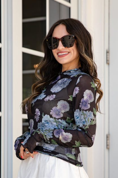Woman wearing a floral blouse and sunglasses outdoors.