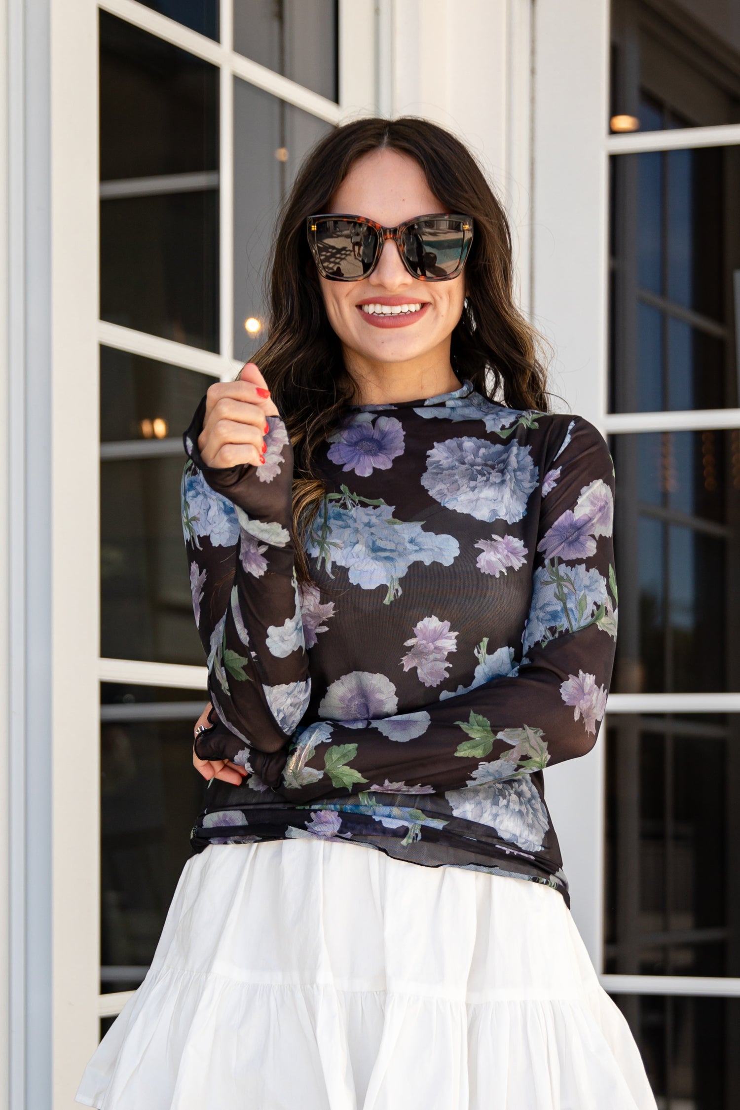 Woman wearing a floral blouse and sunglasses, standing in front of a glass door.