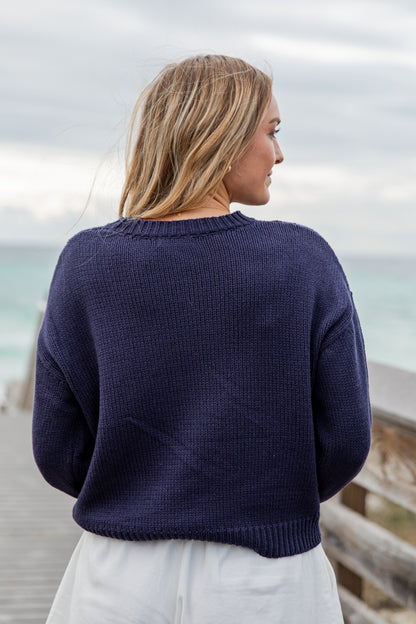Woman wearing a navy blue sweater standing on a wooden deck with a blurred background
