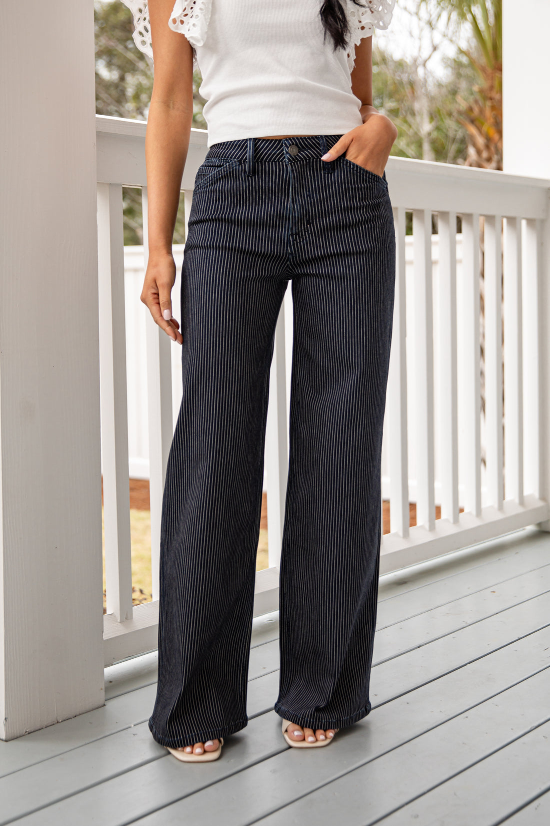Person wearing black pinstripe pants and a white top on a wooden deck.