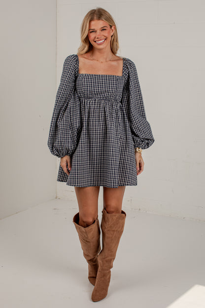 A woman modeling a black and white gingham mini dress with puff sleeves and a square neckline, paired with brown suede knee-high boots, in a bright white studio setting.