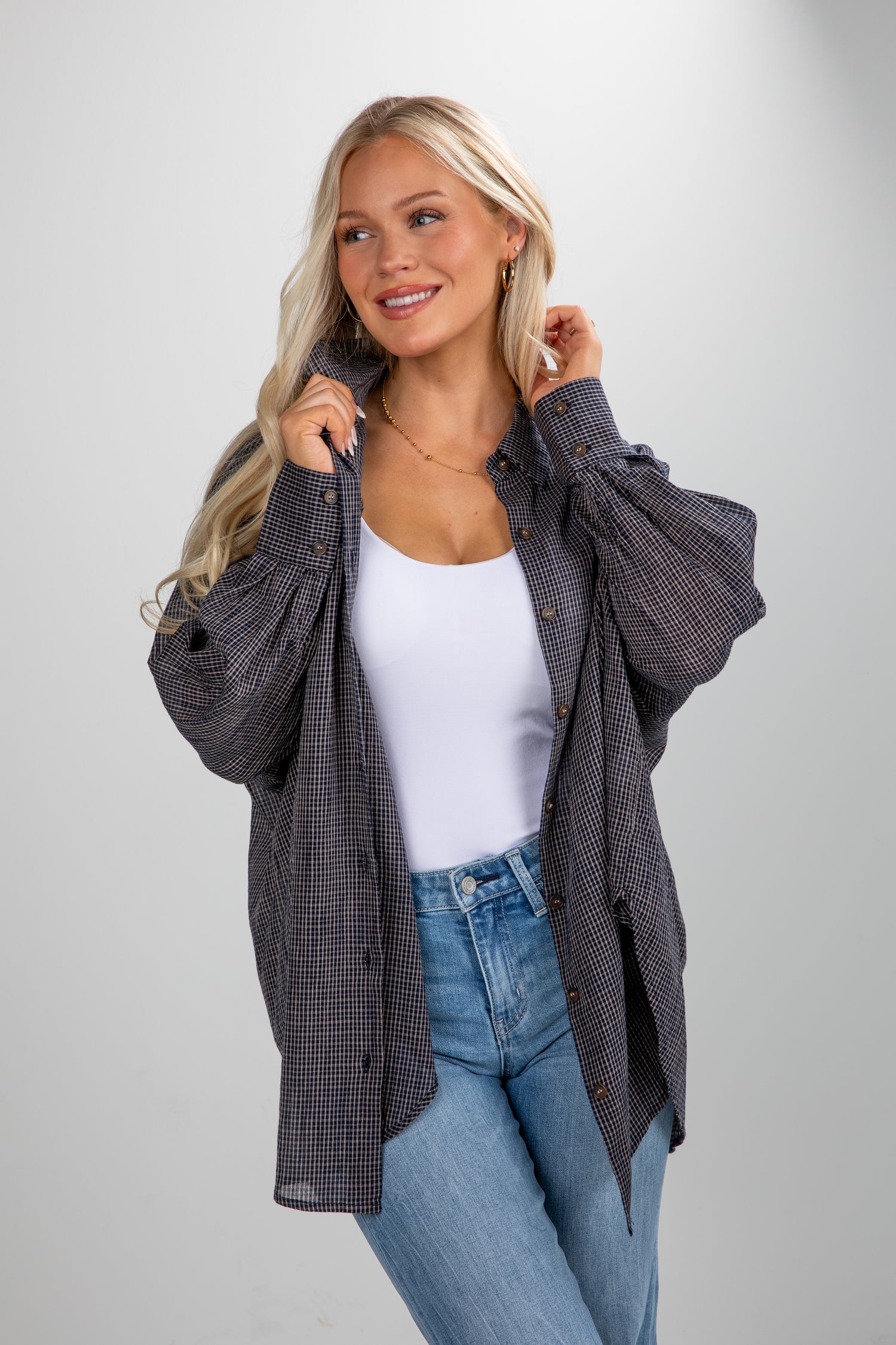 Woman wearing a plaid shirt over a white top and blue jeans on a gray background
