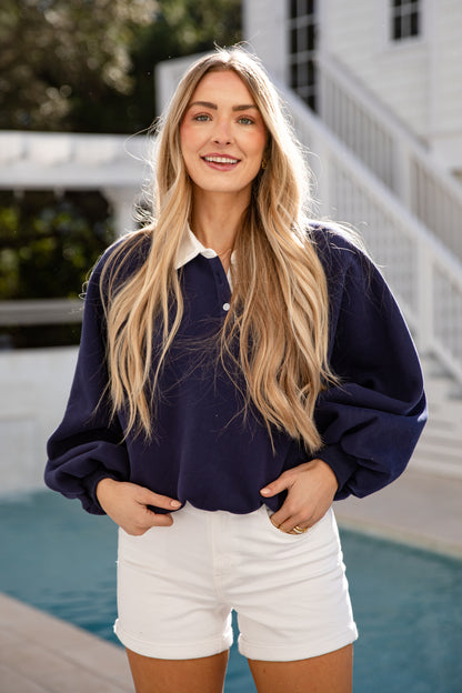 Woman wearing a navy sweater and white shorts by a pool